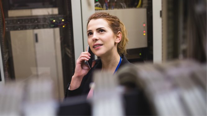 woman standing amid server racks, talking on the phone